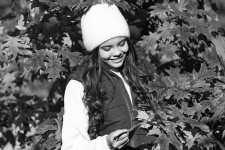 Child teen girl in autumn fall park outdoor, autumn fun kids face. happy child in hat at autumn leaves on natural backgroundの写真素材