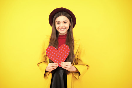 Lovely teenager portrait. Teenage girl hold shape heart, heart-shape sign. Child holding a red heart love holiday valentine symbol. Smiling girl.の写真素材