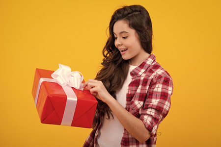 Happy teenager, positive and smiling emotions of child girl. Teenager kid with present box on isolated yellow background. Teen girl giving birthday gift. Present, greeting and gifting concept.の写真素材