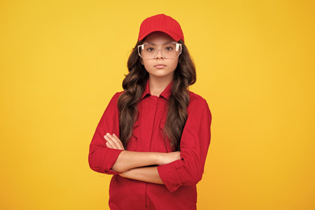 Worker teenager child wearing overalls red, cap and protect glasses. Studio shot portrait isolated on yellow background.の写真素材