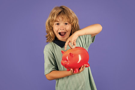 Saving money concept. Kid saving money for purchase, hold pink piggy bank. Child learning to calculate personal budget, manage finance, playing investment, accounting.の写真素材