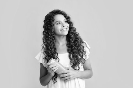 Happy portrait of child teen girl with shampoos conditioners and shower gel. Long hair care of teenager. Presenting cosmetic product, shampoo bottle. Smiling girl.の写真素材