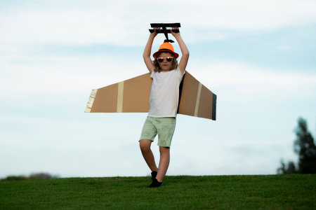 Happy kid playing with toy paper wings outdoors in summer field. Travel and kids vacation concept. Imagination and freedom.の写真素材