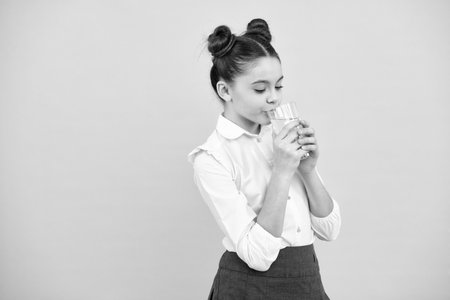 Teenage girl drinking water from glass on blue background. Daily life health. Drink water for health care and body balance. Thirsty child, dehydration.の写真素材