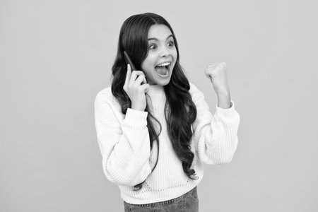 Excited teenager girl 12, 13, 14 years old with smart phone. Hipster teen girl types message on cellphone, enjoys mobile app. Kid hold smartphone texting in online social media. Internet addiction.の写真素材