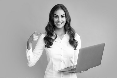 Portrait of a cheerful young casual girl standing isolated over gray background, using laptop computer. Business woman at work.の写真素材
