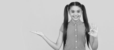 happy kid presenting product on yellow background copy space show ok, advertise. Child face, horizontal poster, teenager girl isolated portrait, banner with copy space.の写真素材