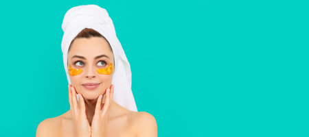 Woman with beauty face, facial skin portrait. smiling young woman has collagen golden eye patches on face with towel. Beautiful woman isolated face portrait, banner with mock up copy space.の写真素材