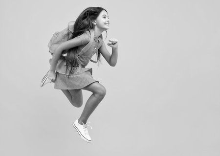 Back to school. Teenage school girl ready to learn. Crazy run and jump. School children on yellow isolated background.の写真素材