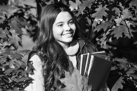 Autumn teen child portrait. happy girl hold workbook on autumn leaves background