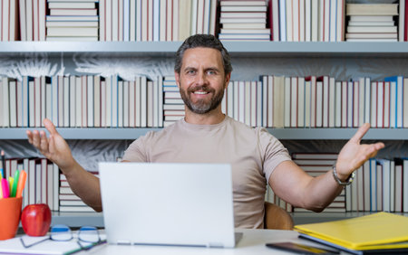 Teacher work on laptop in classroom. Knowledge and education with handsome teacher. Teacher with book in classroom. Man on lesson in class. Teachers from university exam. College teacher.の写真素材