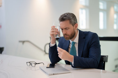 Millennial Businessman in office having headache. Business man in suit work on laptop at home office take off glasses suffer from migraine headache. Man taking a Medicine pill from headache migraine.の写真素材