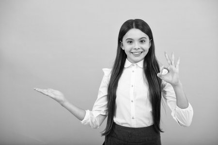 Positive teenager child points aside with cheerful expression, shows amazing at blank empty space. Advertisement and mockup.の写真素材