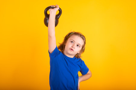 Sporty kids, studio isolated portrait on yellow background. Cute little girl doing exercises with kettlebell. Portrait of sporty child with dumbbells. Happy child girl exercising.の写真素材