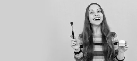 Happy kid apply cosmetics with foundation brush yellow background, makeup. Cosmetics for teenager child, poster design. Beauty kids makeup, banner with copy space.の写真素材