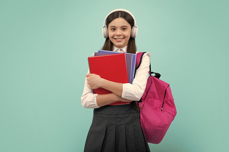 Back to school. Teenager school girl with backpack and headphones hold books ready to learn. School children on isolated blue studio background.の写真素材