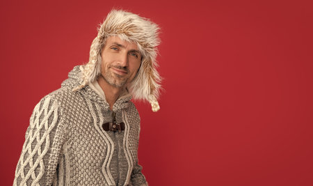 hoary man in sweater and earflap on red background, winter fashion