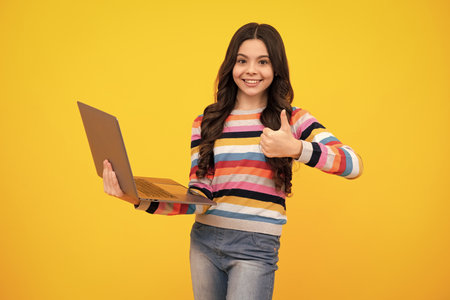 Young girl student hold computer. Funny pupil with laptop isolated on yellow background. Back to...