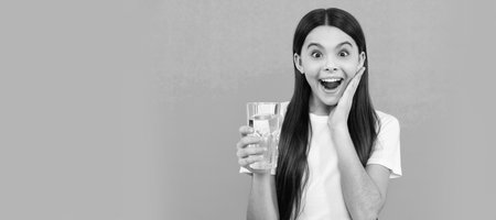 surprised child drink water to stay hydrated and keep daily water balance in body. Banner of child girl with glass of water, studio portrait with copy space.の写真素材