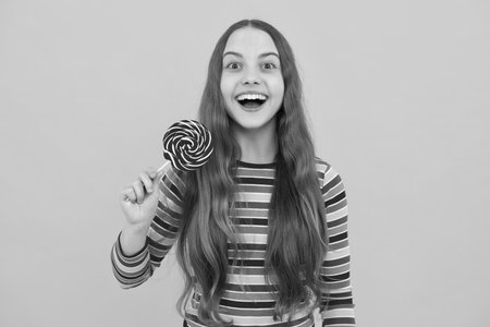 Funny child with lollipop over yellow isolated background. Sweet childhood life. Teen girl with yummy caramel lollipop, candy shop. Teenager with sweet sucker.の写真素材