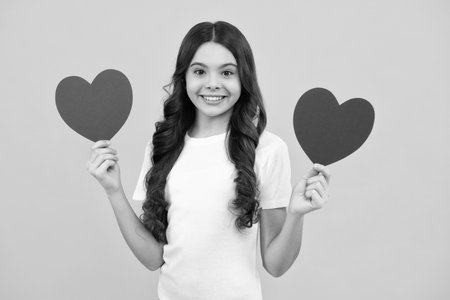 Teenage girl hold shape heart, heart-shape sign. Child holding a red heart love holiday valentine symbol, isolated on yellow background. Happy teenager, positive and smiling emotions of teen girl.の写真素材