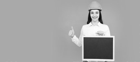 Smiling woman builder in helmet holding board for advertising sign. Sign board with copy space. Woman isolated face portrait, banner with mock up copyspace.の写真素材