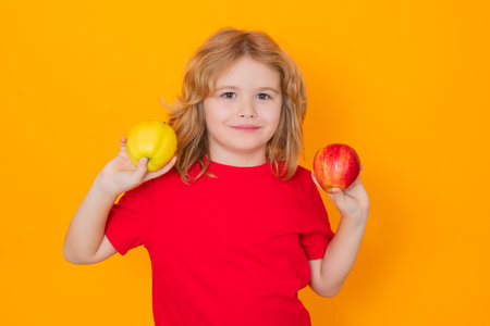 Kid in red t-shirt with apple in studio. Studio portrait of cute child hold apple isolated on yellow...