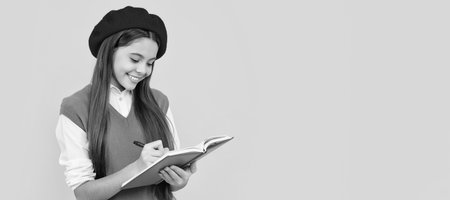 happy teen school girl in french beret making notes in planner notepad or notebook. Portrait of schoolgirl student, studio banner header. School child face, copyspace.の写真素材