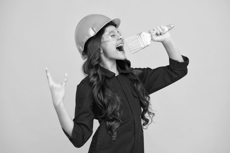 Kids renovation and building concept. Little girl in protective helmet and paint brush for painting walls isolated on yellow background. Excited teenager girl.の写真素材