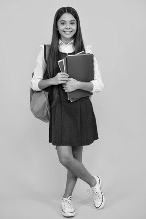 School teenage girl with school bag backpack hold book on yellow isolated studio background. Children school and education concept.の写真素材