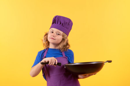 Kid cook with cooking pan. Child wearing cooker uniform and chef hat preparing food on kitchen, studio portrait. Cooking, culinary and kids food concept.の写真素材