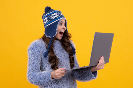 School girl teenager child student in warn hat hold laptop, isolated background. Learning and knowledge education concept. Excited teenager girl.の写真素材