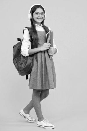 Full length of teenager school girl with backpack holding a book ready to learn. School children with school bag on isolated studio background. Happy face, positive and smilingの写真素材