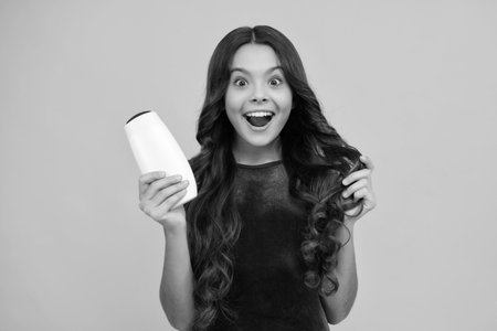 Teenager child girl with bottle shampoo conditioners or shower gel. Kids hair care. Hair cosmetic product, shampoo bottle. Happy girl face, positive and smiling emotions.の写真素材