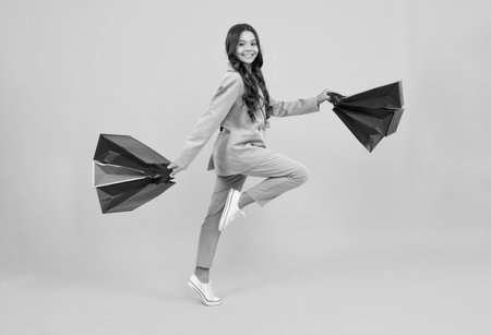 Girl teenager with shopping bags isolated on yellow backgound. Run and jump. Shopping and sale concept.の写真素材