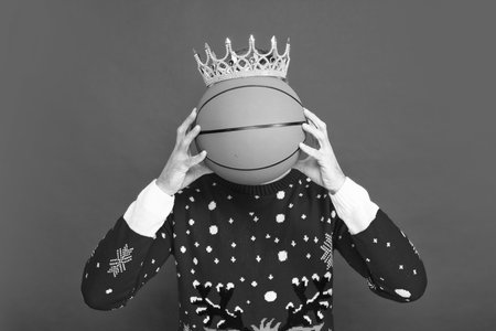 Winter man in crown hold basketball ball. Portrait of christmas santa man on red studio background.の写真素材