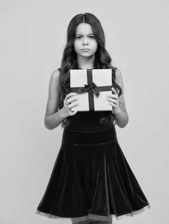 Angry teenager girl, upset and unhappy negative emotion. Teenager child holding gift box on yellow isolated background. Gift for kids birthday. Christmas or New Year present box.の写真素材