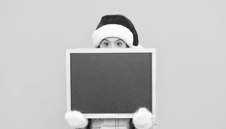 merry christmas. kid in santa hat behind blackboard for copy space. teen girl in mittensの写真素材