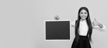 cheerful teen girl in uniform hold school blackboard for copy space showing thumb up, presenting. Banner of schoolgirl student. School child pupil portrait with copy space.の写真素材