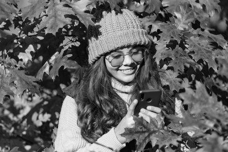 happy kid in sunglasses messaging on smartphone at autumn leaves on natural background