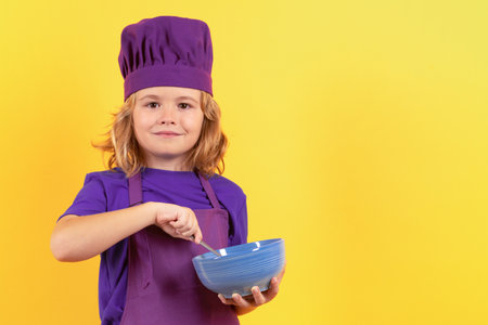 Kid chef cook with cooking bowl. Child chef cook. Child wearing cooker uniform and chef hat preparing food, studio portrait.の写真素材