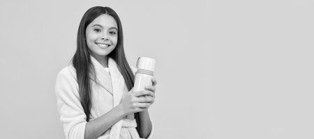happy teen girl in home terry bathrobe with thermos bottle, morning. Horizontal poster of isolated child face, banner header, copy space.の写真素材