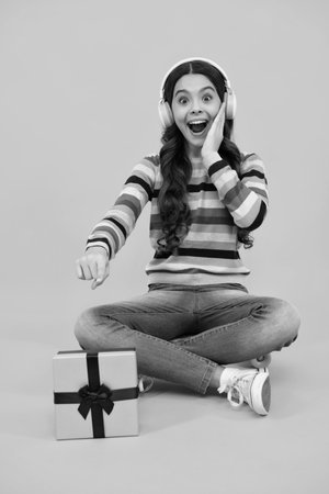 Amazed teenager. Child teen girl 12-14 years old with gift on yellow isolated background. Birthday, holiday present concept. Excited teen girl.の写真素材