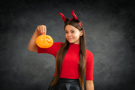 Child with devil horns hold pumpkin. Halloween witch girl. Little girl witch. Kid witch celebrates...