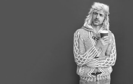 morning coffee in take away cup. serious grizzled guy in sweater and hat on red background.の写真素材