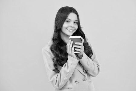 Teenager girl holding a hot cup of coffee or tea. Child with takeaway cup on yellow background, morning energy drink beverage. Happy face, positive and smiling emotions of teenager girl.の写真素材