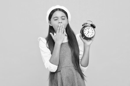 Tired and bored teenager girl. Punctual teen girl checking time. Child with alarm clock showing time.の写真素材