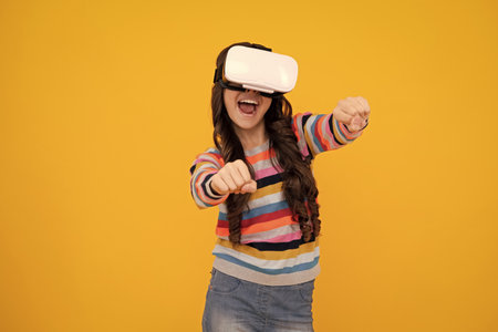 Amazed teenager. Portrait of young teen girl in VR helmet, isolated on yellow. Gamer playing VR...