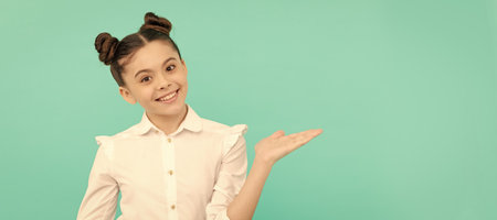 Happy school age child showing open hand for copy space on blue background. Child face, horizontal poster, teenager girl isolated portrait, banner with copy space.の写真素材