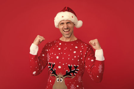 Emotional man in holiday sweater and Santa hat on studio background.